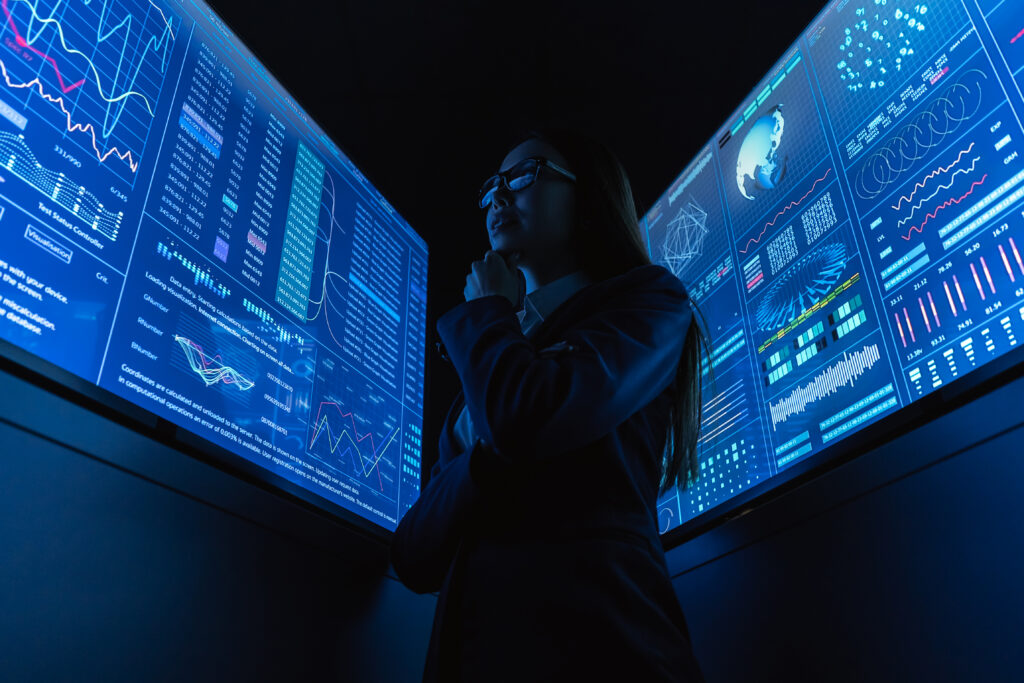 the businesswoman standing near the blue monitor.